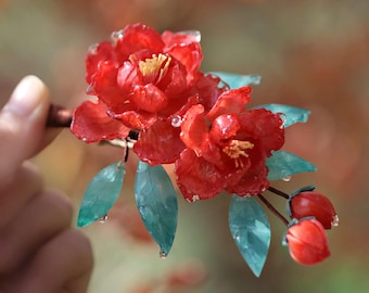May include: A red flower hair clip with green leaves and water droplets. The flower is made of resin and has a realistic appearance.