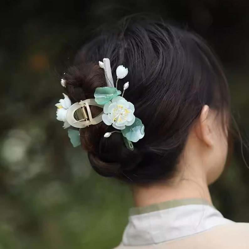 May include: A hair clip with white and green flowers. The clip is made of metal and has a decorative design. The flowers are made of plastic and have a realistic look.