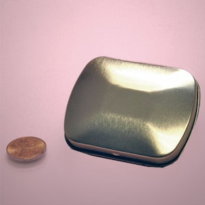 May include: A silver metal tin with a slightly rounded rectangular shape. The tin has a brushed finish and is empty.