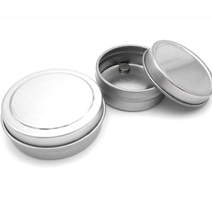 May include: Three small, round, silver-colored metal tins. One tin is open, revealing a small magnet inside. The lids are slightly domed. The tins are empty and appear to be new.