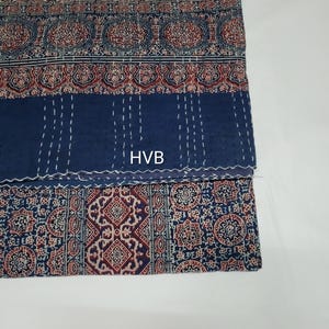 May include: A blue and white kantha quilt with a red and white floral pattern. The quilt is folded in half and the label "HVB" is visible.