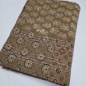 Puede incluir: Tela doblada con un patrón repetitivo de diseños florales y geométricos en tonos marrón, beige, negro y rojo. La tela tiene una textura acolchada y las letras "HVB" son visibles.