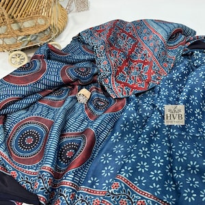 May include: A blue textile with intricate patterns in red and white. The fabric features floral and geometric designs, with a logo in the lower right corner. A decorative ring is placed on the fabric.