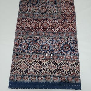 May include: A blue and red patterned cotton quilt with a white background. The quilt has a geometric design and is hand-stitched. The quilt is folded in half and is lying on a white surface. The text "HVB" is visible in the centre of the quilt.