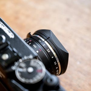 Puede incluir: Una c&aacute;mara negra con un anillo de lente plateado. El anillo de lente tiene marcas para ajustes de apertura de f/1.0 a f/11.