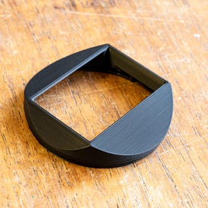 Puede incluir: Un parasol de lente de pl&aacute;stico negro con una abertura cuadrada y un borde redondeado.