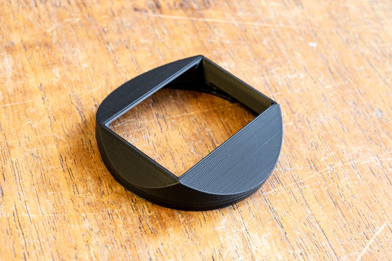 Puede incluir: Un parasol de lente de pl&aacute;stico negro con una abertura cuadrada y un borde redondeado.