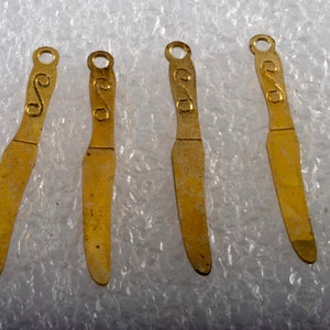 May include: Four gold-colored metal knife-shaped charms with a decorative swirl design on the handle.