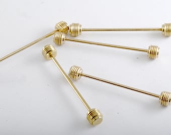 May include: Six gold tie bars with a textured, ribbed design on the ends. The tie bars are arranged in a fan shape on a white surface.