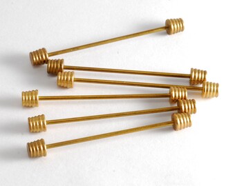 May include: A set of eight gold-toned tie tacks with a decorative, ridged design. The tacks are arranged in a fan shape on a white surface.