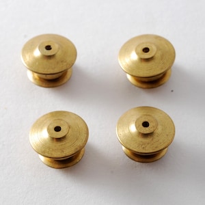May include: Four gold-colored metal pin backs with a small hole in the center of each. The pin backs are round and have a slightly raised edge.