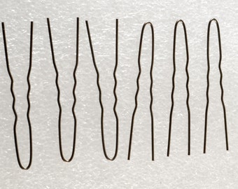 Puede incluir: Siete horquillas de color marrón oscuro dispuestas sobre una superficie blanca. Las horquillas tienen un diseño ondulado en los lados y una parte superior redondeada. Estos accesorios para el cabello se utilizan para sujetar el cabello.