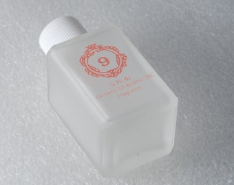 May include: A clear glass bottle with a white cap and a pink label. The label has a number 9 inside a decorative circle and the text "1/2 Fl Oz Contains SD Alcohol 39C Fragrance".