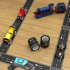 May include: Toy cars and a train travel on a road made of black tape with white lines, arrows, and crosswalks. The tape is on a wooden surface. The image includes the text "OTO BANT" and "go!"