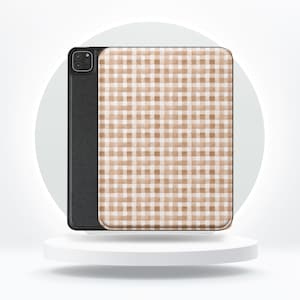 May include: A black tablet case with a tan and white gingham pattern. The case is shown on a white pedestal against a white background. The case has a camera cutout on the back.