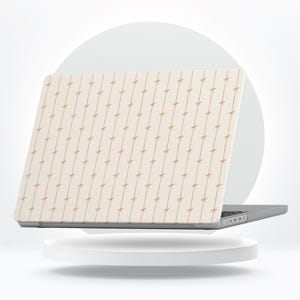 Può includere: Laptop con custodia color crema con un motivo ripetuto di linee verticali con piccoli fiocchi marrone chiaro. Il laptop è posizionato su una piattaforma bianca e circolare su uno sfondo bianco.