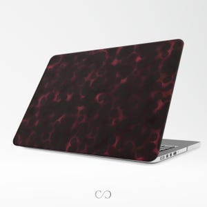 May include: A laptop computer with a burgundy and black spotted design on the lid. The pattern has a mottled appearance with dark and light areas. The laptop is open, revealing the keyboard and screen.