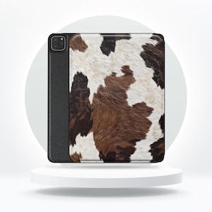 Op de afbeelding: Tablethoesje met een koeienhuidpatroon. De hoes heeft een zwarte rand en een getextureerde achterkant met bruine, zwarte en witte vlekken. De hoes is ontworpen om de tablet te beschermen.