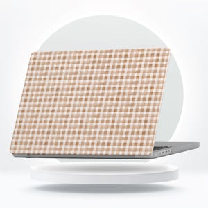 May include: A laptop with a tan and white gingham pattern on the lid. The laptop is open, displaying the screen, and is set on a white platform. The gingham pattern is a classic design.