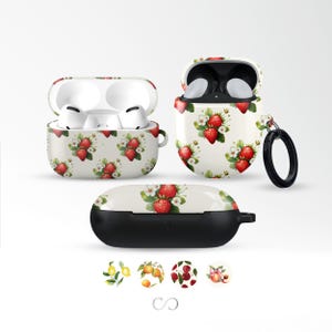 May include: White AirPod cases with a strawberry pattern. The cases are open and closed, showcasing the earbuds inside. The design features red strawberries, white flowers, and green leaves on a cream background. A black ring is attached to one case.