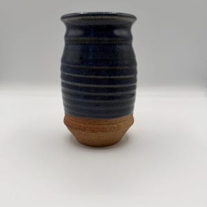 May include: A handmade ceramic vase with a dark blue glazed top and a textured, ridged design. The base is a natural, unglazed terracotta color. The vase has a cylindrical shape with a slightly flared rim, perfect for displaying flowers or as a decorative piece.