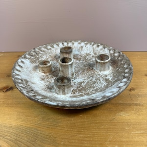 May include: A round ceramic candle holder featuring a mottled brown and white glaze. The surface has a textured, speckled appearance with four cylindrical candle sockets arranged in a cluster toward the center of the shallow, plate-like base.