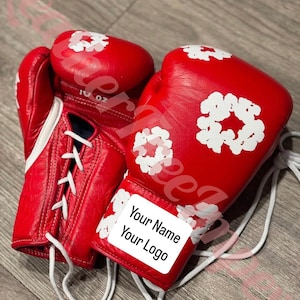 May include: Pair of red boxing gloves with white floral designs. The gloves have white laces and a white label that says "Your Name Your Logo". The gloves are 10 oz.