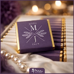 May include: A close-up of a purple chocolate bar with gold foil edges. The bar is personalized with the names "Mary" and "Jack" and the initial "M" and "J" with a floral design. The chocolate bars are arranged in a white box with a pearl necklace.