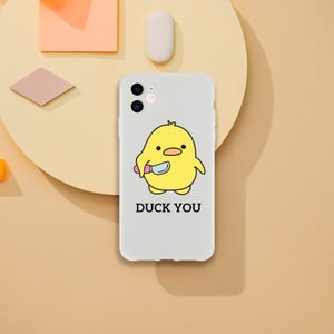May include: A white phone case with a yellow cartoon duck holding a knife. The text "DUCK YOU" is printed below the duck.