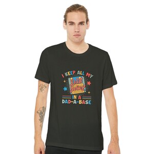Peut inclure: Un t-shirt noir avec un graphique de disquette de style rétro et le texte "I keep all my dad jokes in a dad-a-base".