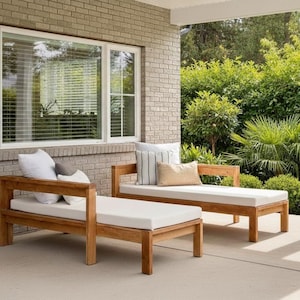 Może przedstawiać: Dwa drewniane leżaki z białymi poduszkami ustawione na betonowym patio. Leżaki mają prosty, nowoczesny design. Na leżakach umieszczono poduszki w różnych kolorach i wzorach. Tło przedstawia ceglaną ścianę i bujną zieleń.