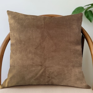 May include: A brown velvet pillow on a wooden chair. The pillow is square and has a smooth, soft texture.