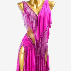 Puede incluir: Vestido de baile fucsia con escote en V y flecos. El vestido presenta una abertura alta y est&aacute; adornado con detalles brillantes. Incluye una pieza de hombro drapeada, creando una silueta elegante.