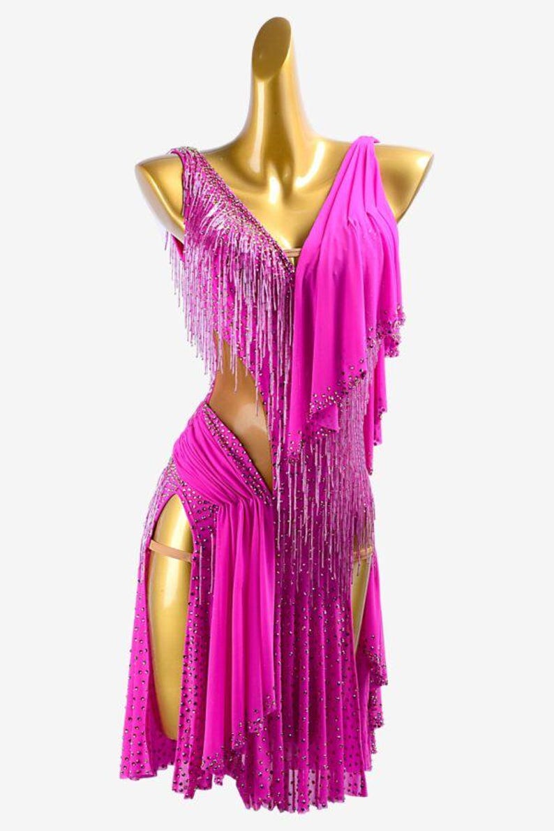 Puede incluir: Vestido de baile fucsia con escote en V y flecos. El vestido presenta una abertura alta y est&aacute; adornado con detalles brillantes. Incluye una pieza de hombro drapeada, creando una silueta elegante.