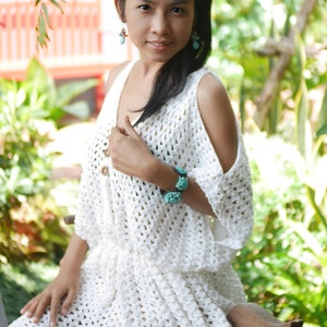 May include: A white crochet dress with a scoop neck and cold shoulder design. The dress has a loose fit and is made with a delicate open stitch pattern.