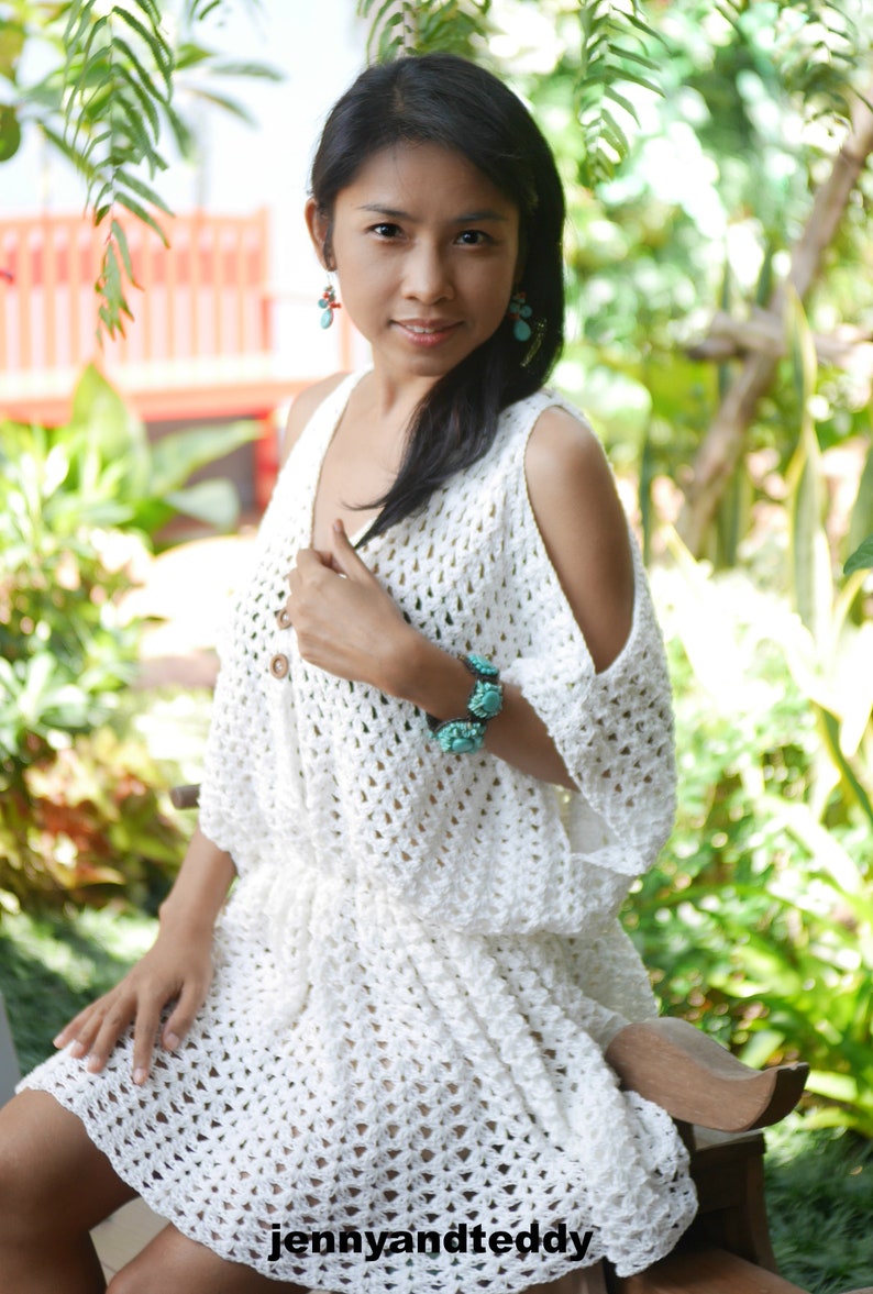 May include: A white crochet dress with a scoop neck and cold shoulder design. The dress has a loose fit and is made with a delicate open stitch pattern.