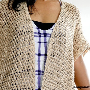 May include: A beige crochet cardigan with a loose, open-weave pattern. The cardigan has short sleeves and a V-neck.
