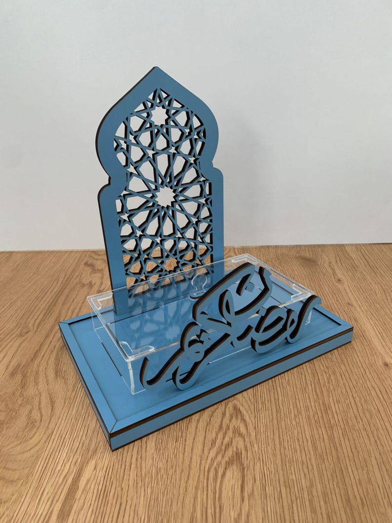 May include: A blue wooden decorative piece with an arched top featuring a geometric pattern. The base has a clear acrylic shelf and a script in black. The piece is designed for display.