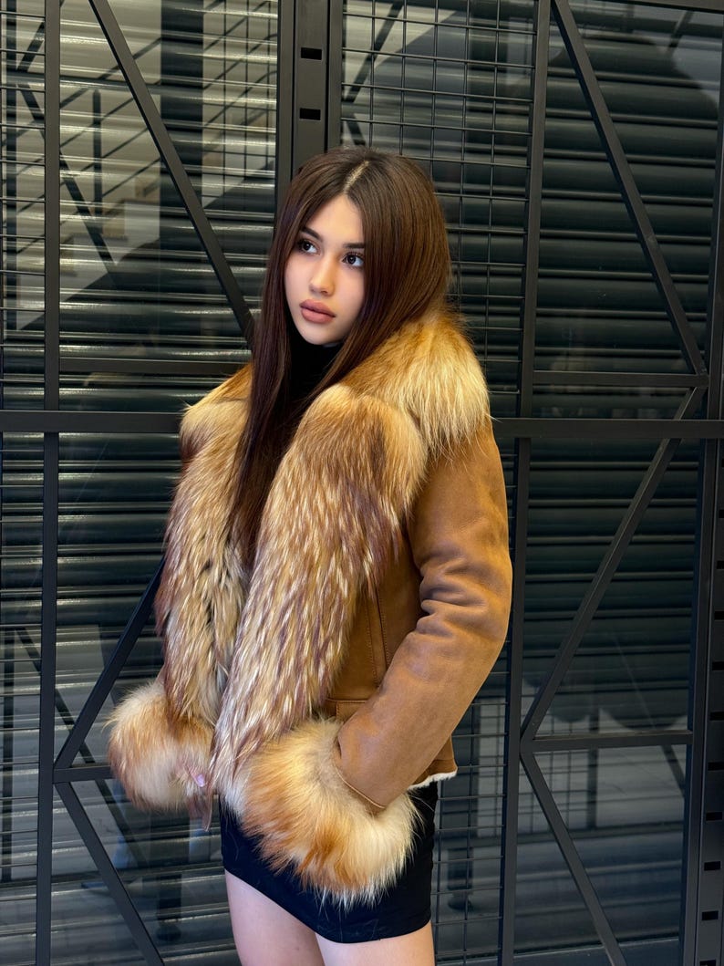 K&ouml;nnte beinhalten: Braune Wildlederjacke mit Pelzkragen und Manschetten. Die Jacke hat ein klassisches Design mit einem warmen, einladenden Aussehen. Der Pelzbesatz verleiht der Oberbekleidung einen Hauch von Luxus und Raffinesse.