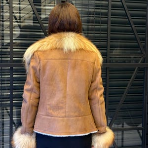 K&ouml;nnte beinhalten: Braune Jacke aus Kunstwildleder mit beigem Pelzkragen und -b&uuml;ndchen. Die Jacke hat ein klassisches Design mit taillierter Passform. Der Pelzbesatz sorgt f&uuml;r einen Hauch von Luxus. Die Jacke wird &uuml;ber einem schwarzen Minirock getragen.