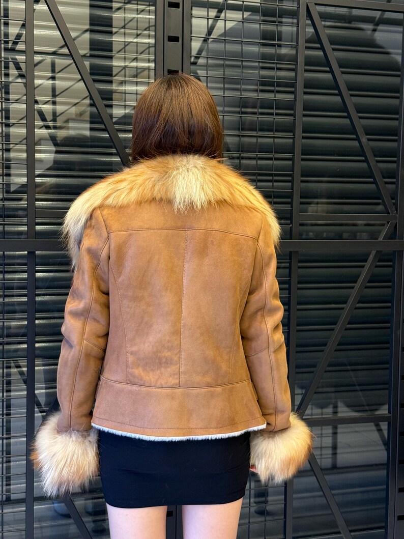 K&ouml;nnte beinhalten: Braune Jacke aus Kunstwildleder mit beigem Pelzkragen und -b&uuml;ndchen. Die Jacke hat ein klassisches Design mit taillierter Passform. Der Pelzbesatz sorgt f&uuml;r einen Hauch von Luxus. Die Jacke wird &uuml;ber einem schwarzen Minirock getragen.