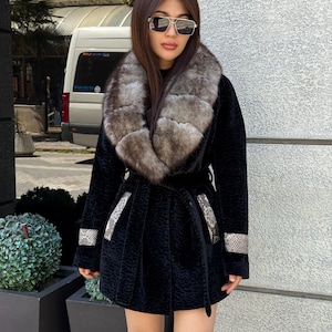 May include: A black coat with a faux fur collar and a matching belt. The coat features decorative silver accents on the cuffs and pockets. The coat is knee-length and has a textured pattern.
