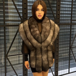 May include: A woman wearing a luxurious, grey and brown fur stole. The stole is draped over a black dress and has a plush, textured appearance. The background features a dark, geometric pattern.