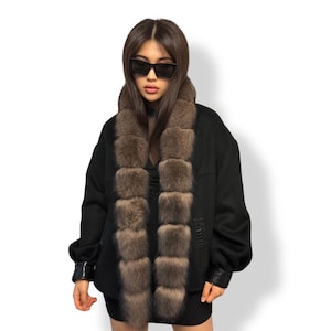 Könnte beinhalten: Schwarze Jacke mit braunem Pelzkragen. Die Jacke hat lange Ärmel und Lederdetails an den Manschetten. Der Pelzkragen besteht aus quadratischen Pelzstücken.