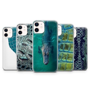 May include: A collection of five clear phone cases featuring various reptile skin patterns and a central alligator graphic. The designs include blue and green textured scales, a dark snake skin print, and a top-down view of an alligator in water.