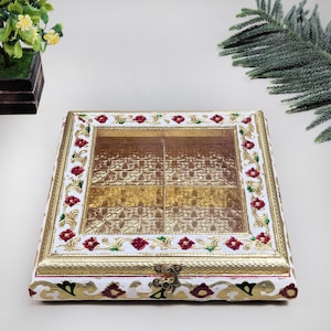 May include: A square, decorative box with a clear top, featuring a gold and white floral design. The box has a gold border and is adorned with red and green floral accents. The interior is divided into four sections.
