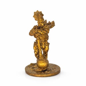 Puede incluir: Una estatua dorada de una deidad, de pie sobre una base circular. La figura está adornada con ropa detallada y un tocado. La estatua sostiene un objeto largo que termina en una olla redonda. Es un artículo religioso o decorativo.