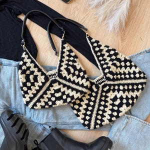 Peut inclure: Deux sacs à main en crochet noir et crème avec des anses noires. Les sacs sont posés sur un jean en denim bleu clair. Des bottes noires et des lunettes de soleil sont également dans l'image. Les sacs ont un motif géométrique.