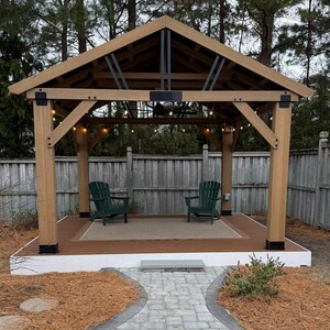 Pode incluir: Um gazebo de madeira com telhado castanho e vigas de suporte. Duas cadeiras Adirondack verdes estão em um deck castanho com um tapete bege. O gazebo é cercado por uma cerca de madeira e um caminho de pedra.