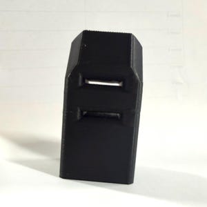 May include: A black, rectangular object with two horizontal rectangular cutouts. The object has a textured surface and appears to be made of a solid material. The item is standing upright.
